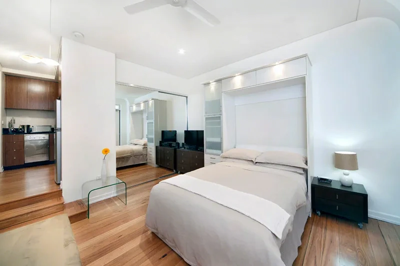 Sleeping area with queen bed and mirrored built-in storage in the Balmain studio
